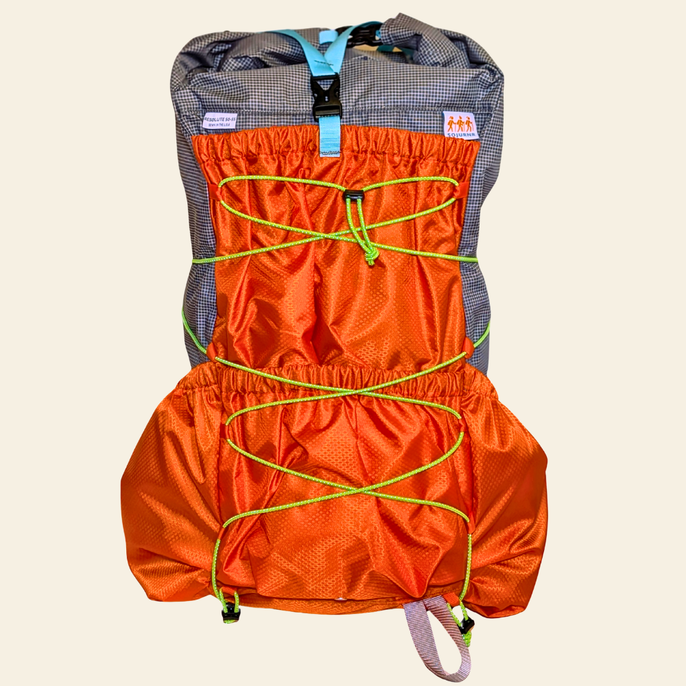 Front view of the Sojurnr Resolute 50-55 women’s ultralight backpack with bright orange pockets, green stretch cord, and a light blue top strap.